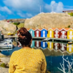 Lady viewing a row of multicoloured huts next to a body of water