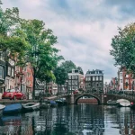 Image of a canal with boats moored either side, and tall buildings on both sides