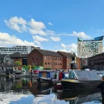 Image of a canal with boats moored in it and large modern buildings in the background