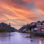 Image of a river with a tall suspension bridge above it and colourful buildings on the right hand side