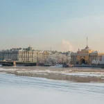 Frozen river with snow covered buildings and trees in the background