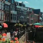 Image of a canal with buildings and people walking next to it
