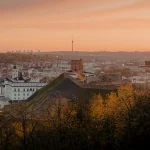 Picture of Vilnius' skyline from the top of a hill, with a orange sunset across the sky