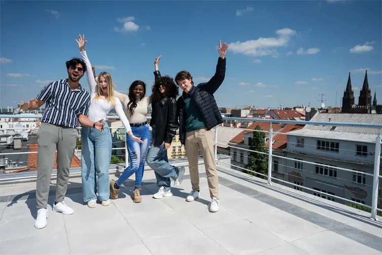 5 students stood on the top of a building with their arms in the air looking happy