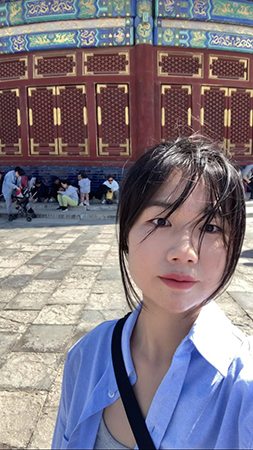 Image of a student standing in front of a large red wall with intricate blue, green and gold decorations on it