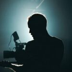Image of a person holding a camera in a dark room with a bright white light shining from behind his head