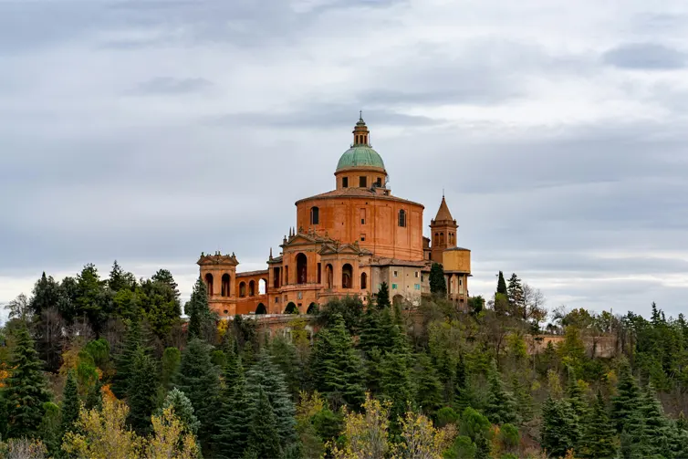 Large red cathedral style building on the top of a tree covered hill.