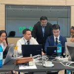 A group of students sat around a table looking at their laptops and each other