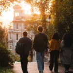 Student walking towards a building with the sun directly behind it