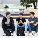 Image of three students sitting on a step and smiling at each other