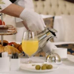 A person's hand with a white glove on serving a drink into a glass
