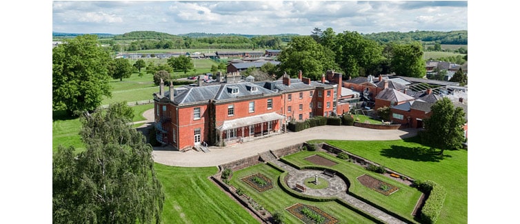 Image of a large red brick building surrounded by green fields and trees