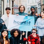 Image of students standing in a street holding a flag that reads 'Howest University of Applied Sciences' smiling at the camera
