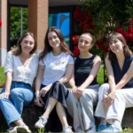 Four students sat on a step smiling at the camera