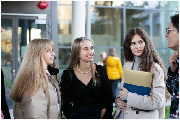 Four students wearing coats looking at each other and smiling