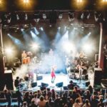 Image of a stage performance with bright lights and people on the stage
