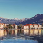 Scenic mountains act as a backdrop to building lining a lakefront shoreline