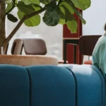 Image of a student sat on a blue sofa with their laptop on their lap
