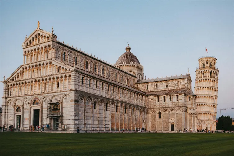 Large sandstone coloured building with the Leaning Tower of Pisa in the background.