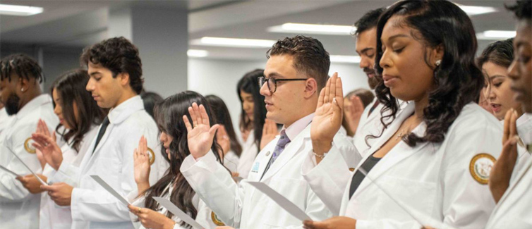 Students wearing white coats swearing an oath with their right hands up.