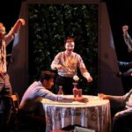 Students on stage in costume, gathered round a table