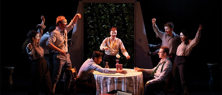 Students on stage in costume, gathered round a table