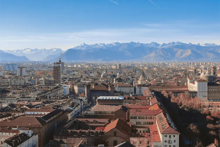 A city skyline of red roofs and a mountain range in the background, with snow on the mountain tops.