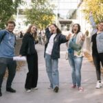 Image of seven students stood in a line with their hands in the air looking happy and excited