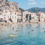 A beach with buildings on the shoreline and people in the sea.