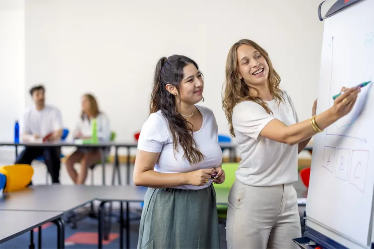 Two students writing on a whiteboard smiling