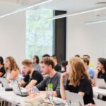 Image of students sat at rows of desks with laptops in front of them